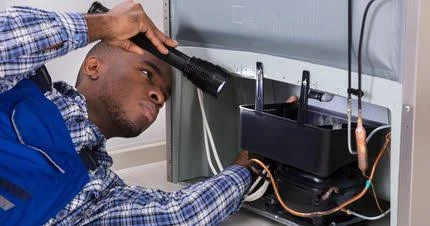 Technician using a flashlight to inspect refrigerator components
